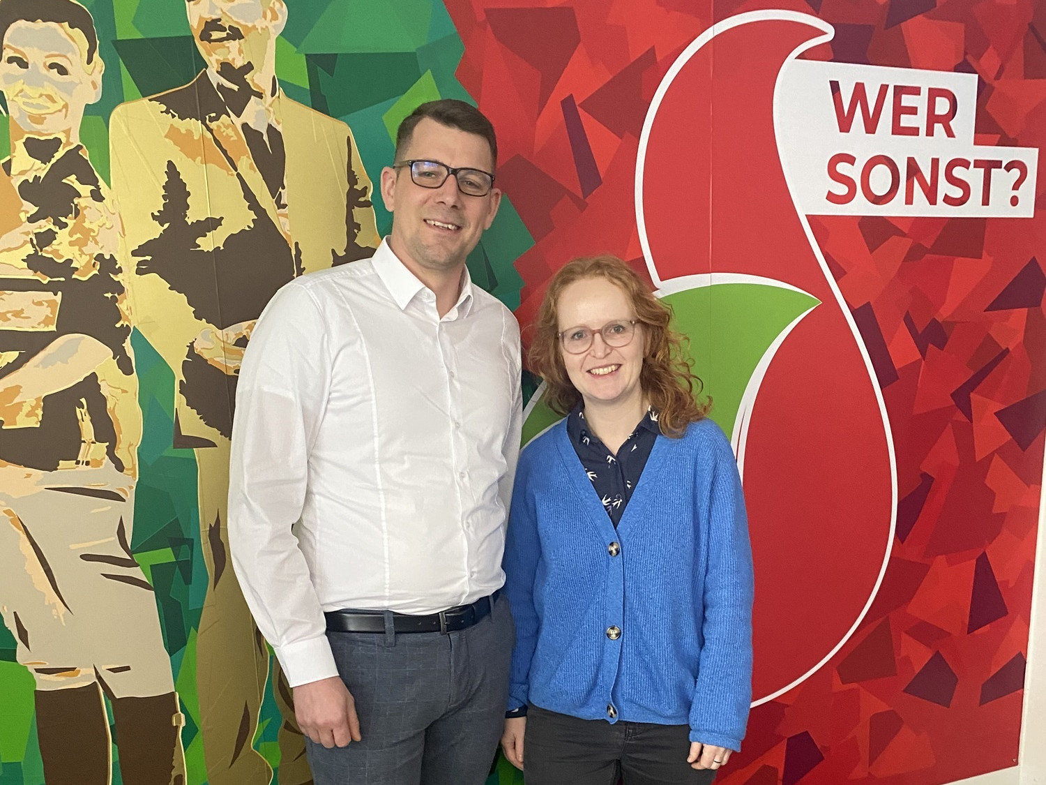 Patrick Lorenz und Linn Grunwald Ein Mann und eine Frau stehen lächelnd vor einer bunten Wand.